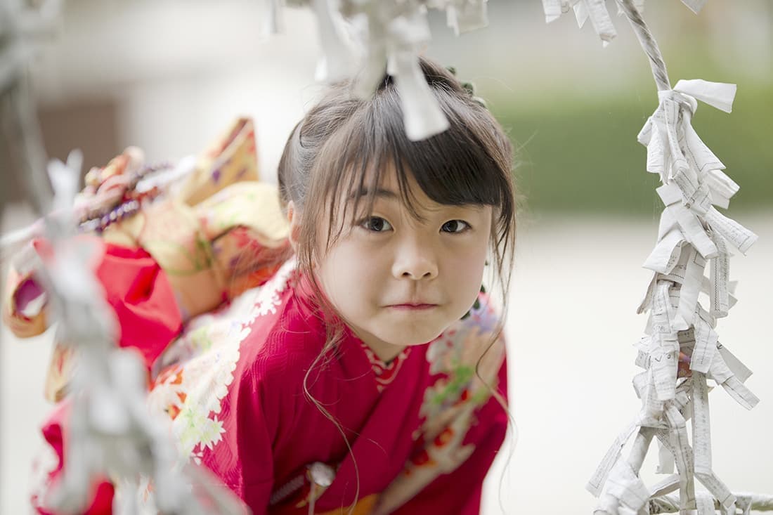 七五三の出張撮影｜5歳の女の子。七五三の撮影。ハートの御神籤を結ぶ所から顔を覗かせて。